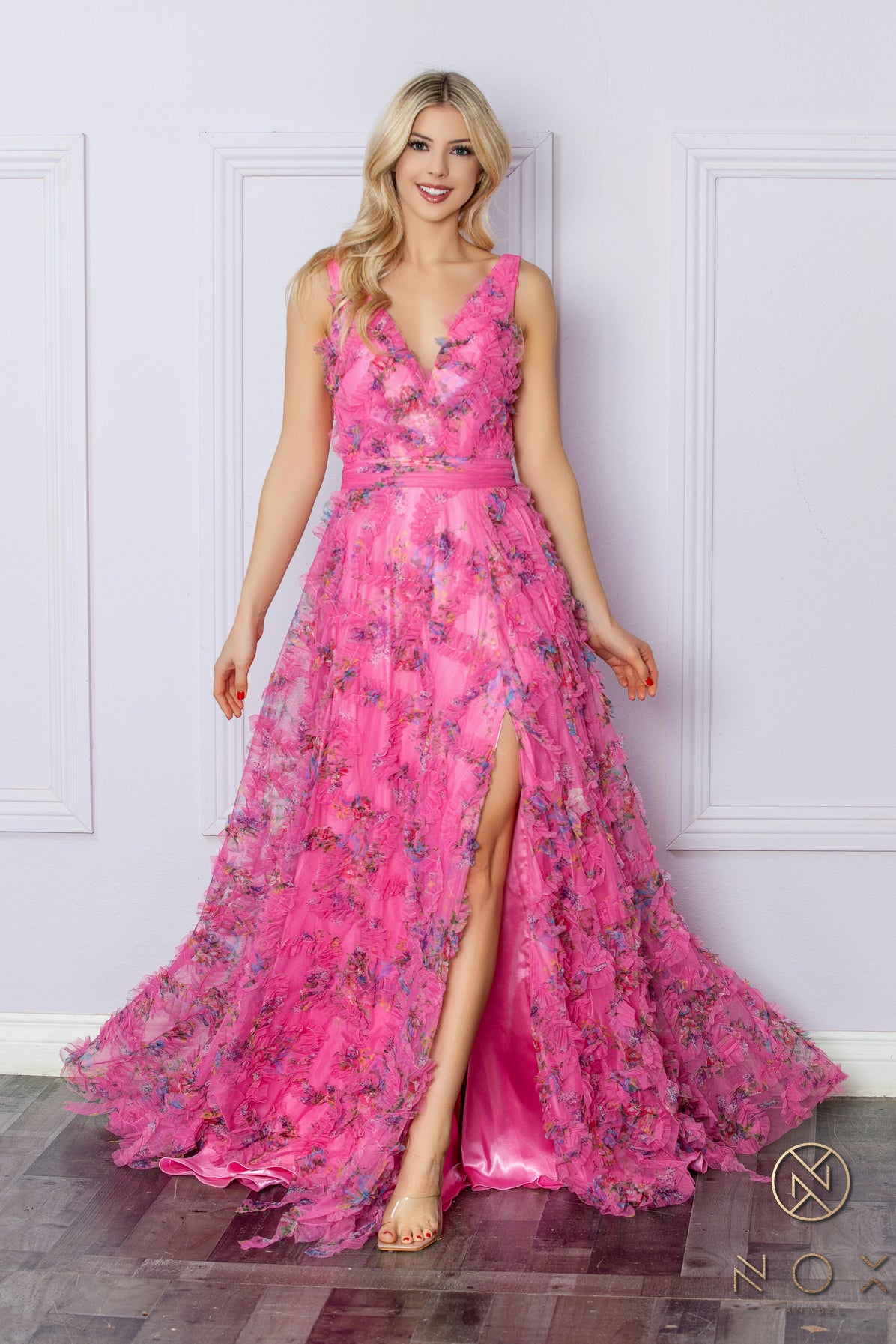 Elevate your formal ensemble with our Nox Anabel E1445 long floral A line dress. Featuring a stunning ruffle detailing and a flattering V neck, this dress is perfect for any prom or formal event. The elegant pleated design and maxi slit add a touch of boho flair to this timeless piece.  Sizes: 2-16  Colors: Blue, Fuchsia, Lilac