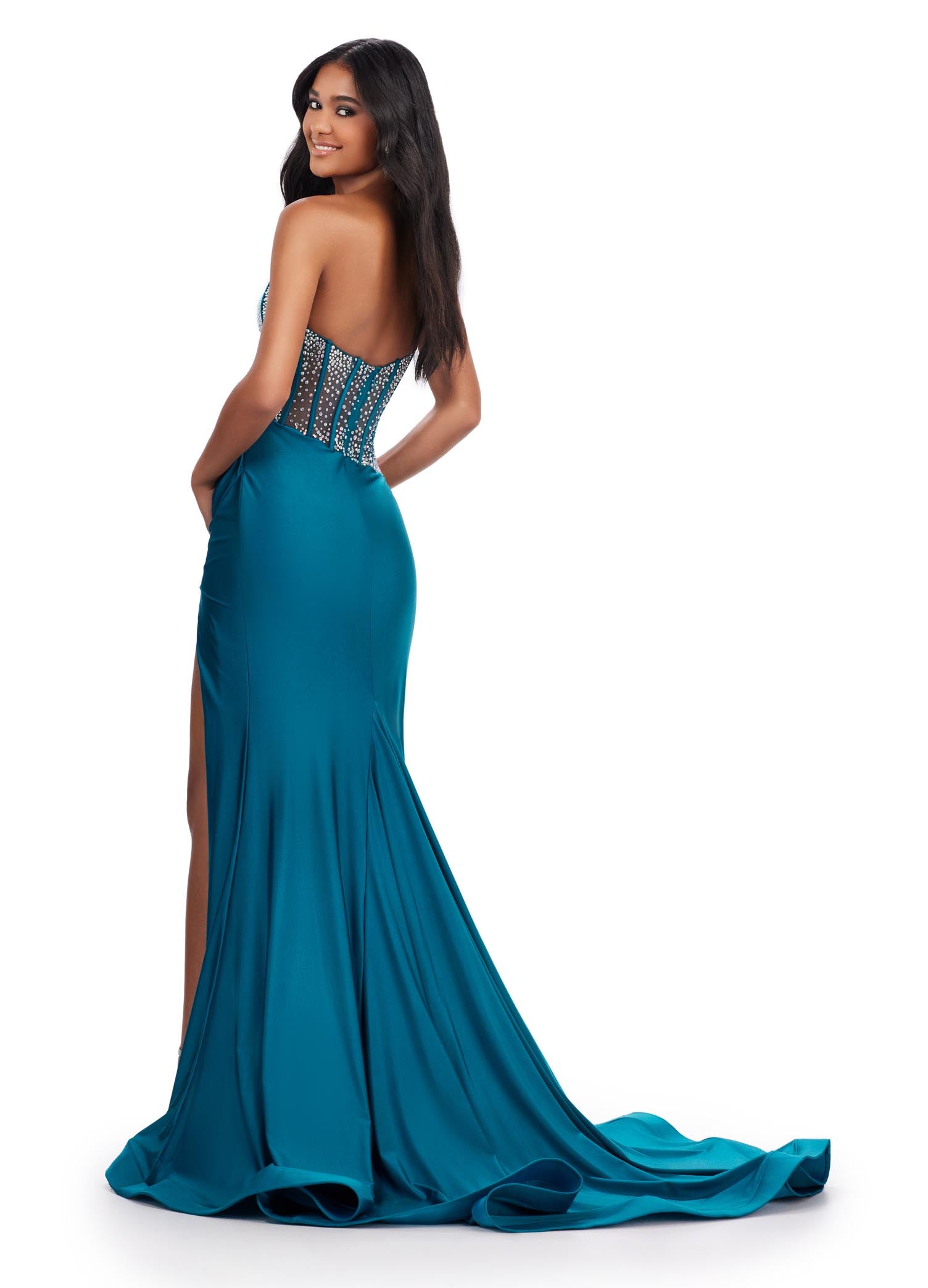 The Ashley Lauren 11617 Evening Gown is crafted from sheer fabric with a one shoulder design adorned with delicate crystal embroidery. The fitted silhouette features a corset bodice with a maxi slit and long train with a voluminous skirt. Perfect for prom, pageants, and formal events. Elegance with a twist! This one shoulder jersey gown features a stunning beaded corset bustier for an added touch of glam.  COLORS: Purple, Magenta, Peacock, Black Sizes: 00-24