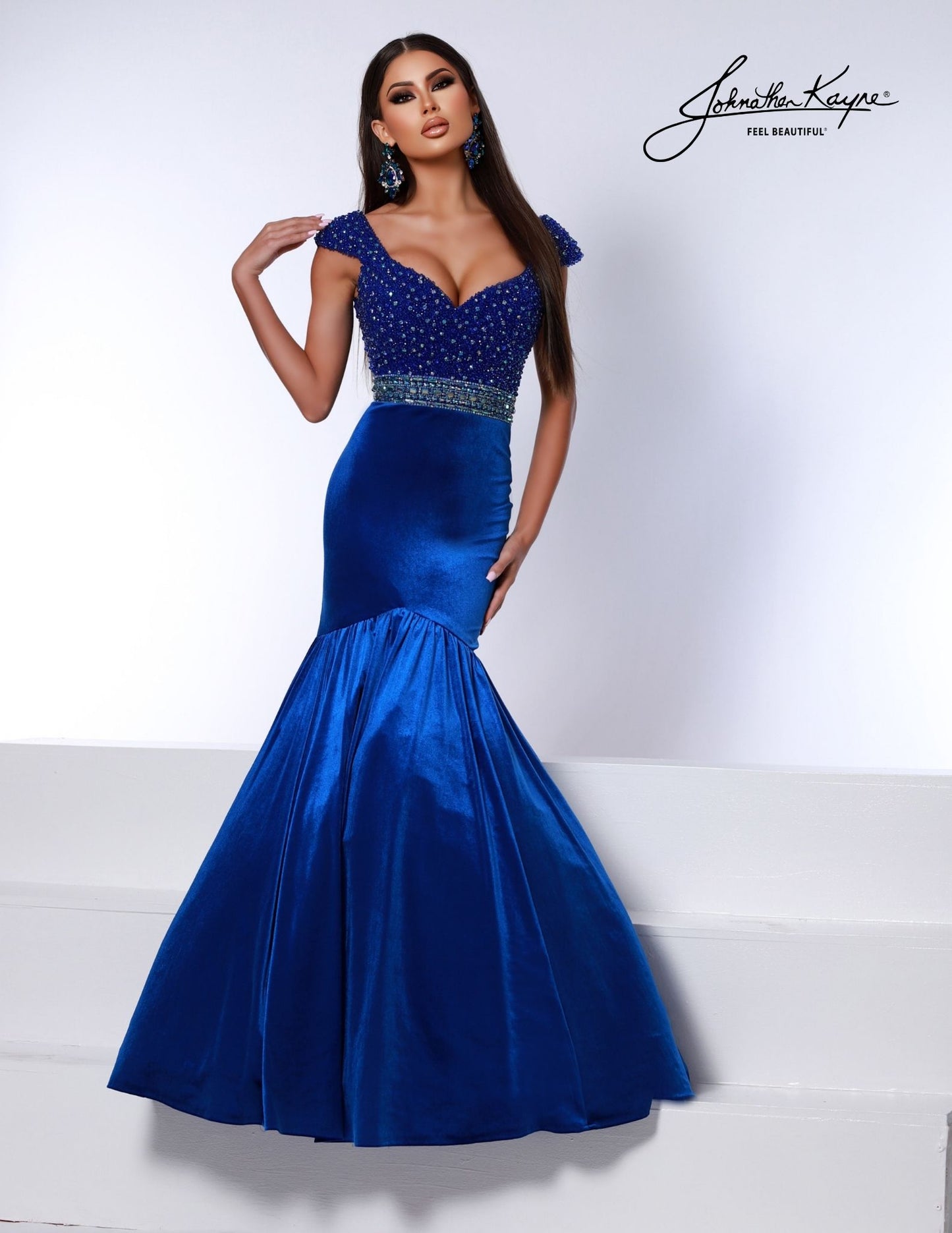 Introducing the Johnathan Kayne 2724 dress; a stunning evening gown featuring a fitted velvet bodice and mermaid skirt. Luxuriously crafted with a hot stone embellishment, it is sure to turn heads at any special event. The look is finished with an eye-catching crystal belt for a show-stopping finish.  Sizes: 00,0,2,4,6,8,10,12,14,16  Colors: Black, Red, White, Royal 