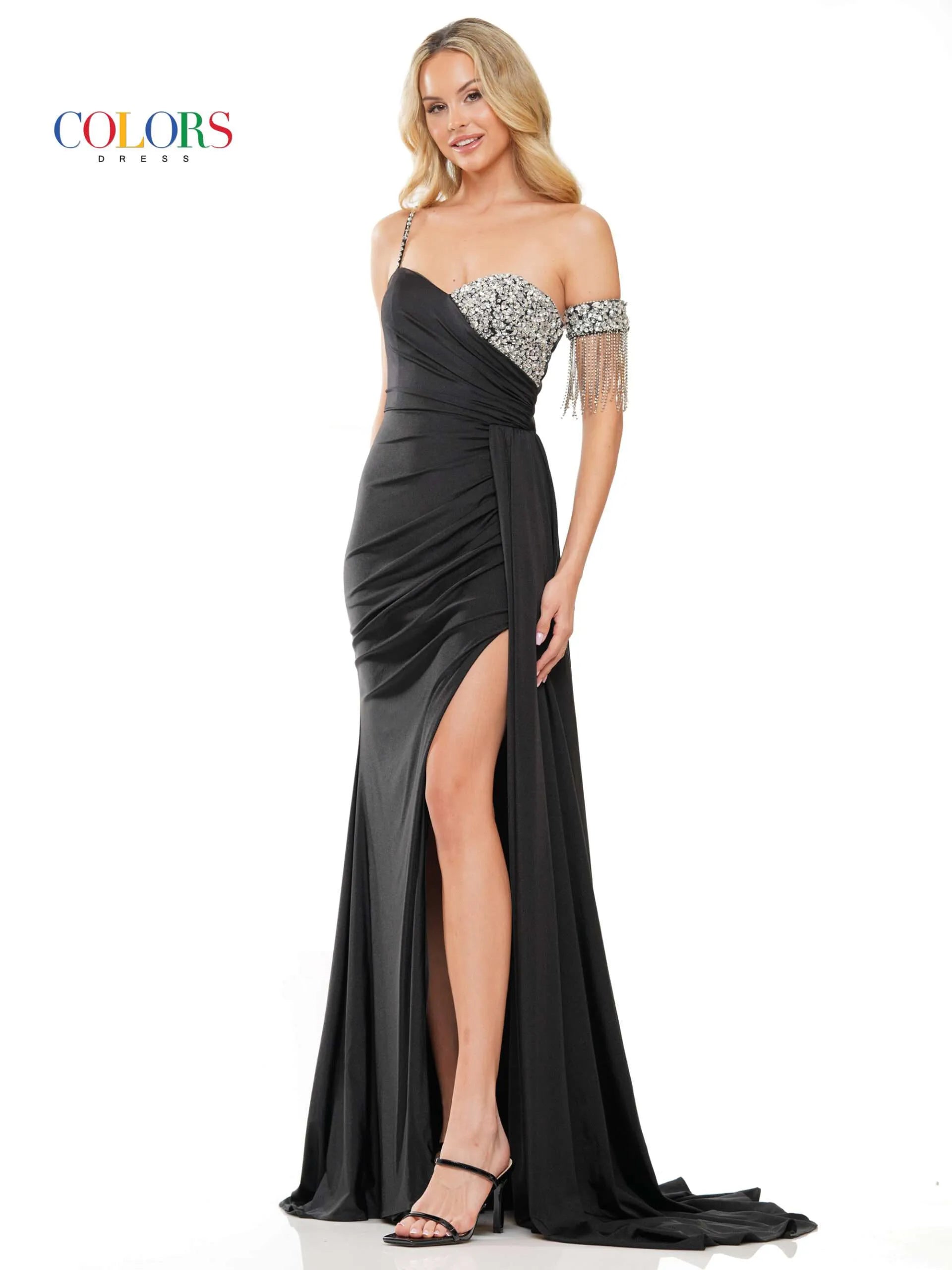 Step onto the red carpet in style with the Colors Dress 3275 Fitted Ruched Slit Overskirt Prom Dress. The one side off the shoulder design is embellished with eye-catching crystal details, while the fitted silhouette is accentuated with a ruched overskirt and fringe detailing. Be the standout at any pageant or prom with this beautiful and glamorous dress.  Sizes: 0-22  Colors: Black, Royal, Deep Green, Hot Pink