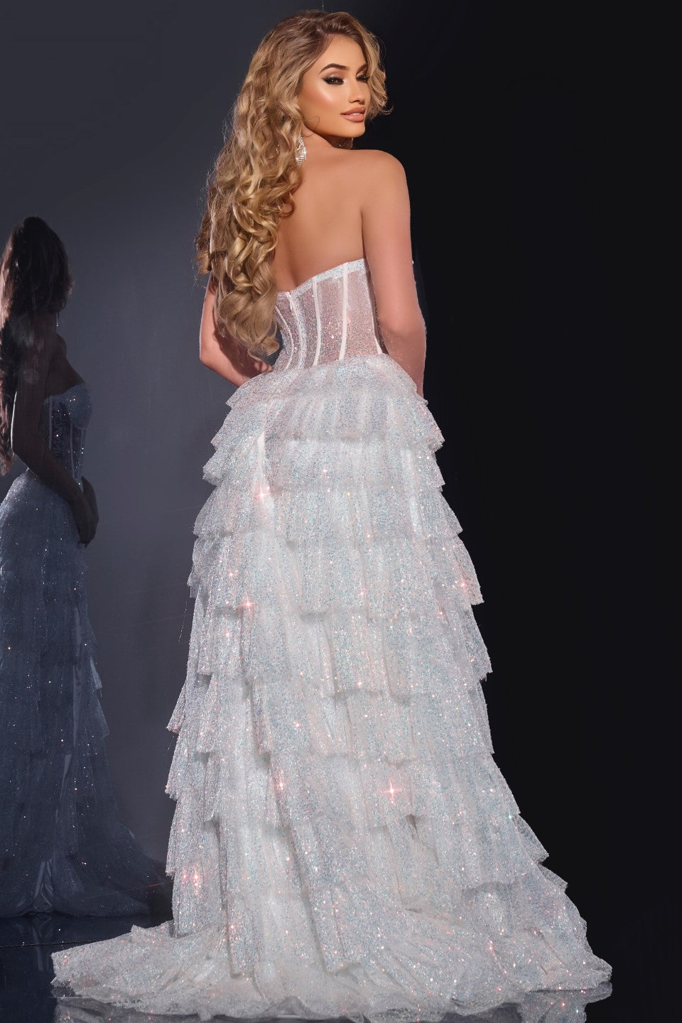 Introducing the Jovani 38165, a remarkable prom dress from the formal collection that's designed to make a lasting impression. Crafted from delicate tulle, this A-line gown is the epitome of elegance and sophistication. Its sequin embellishments add a touch of sparkle and luxury to the ensemble, ensuring you'll shine on your special night.&nbsp;The dress features a layered skirt with a high slit, creating a dramatic and alluring effect. The illusion corset bodice, complete with boning, provides a structured