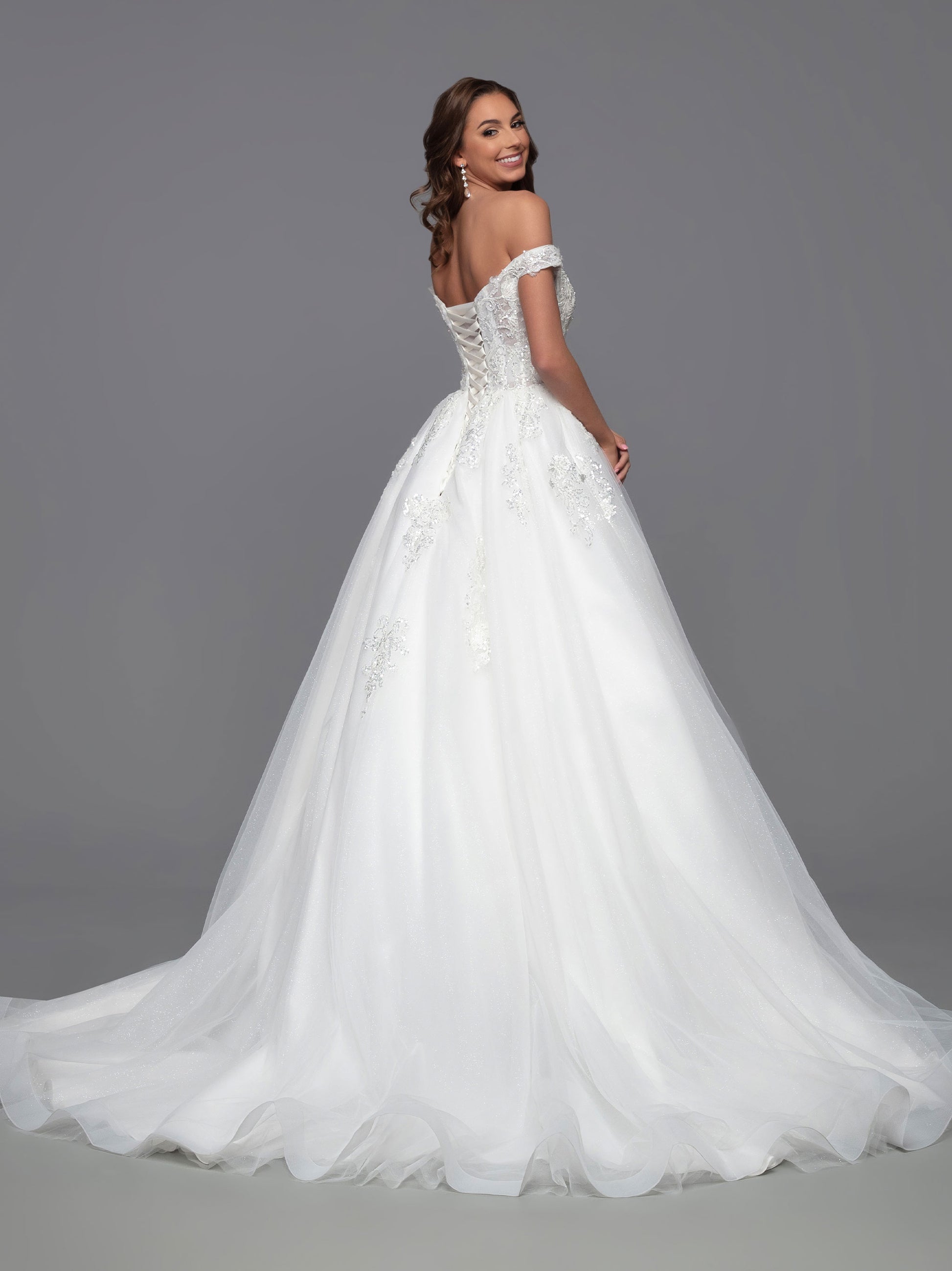 This classic, A-Line ballgown by Davinci Bridal is the perfect combination of timeless elegance and modern touches. The shimmer sheer, off-the-shoulder bodice offers a unique, contemporary look, while the layered tulle skirt features scattered lace accents and a chapel train for a traditional, timeless feel. A corset back ensures a perfect fit.  Sizes: 2-20  Colors: Ivory