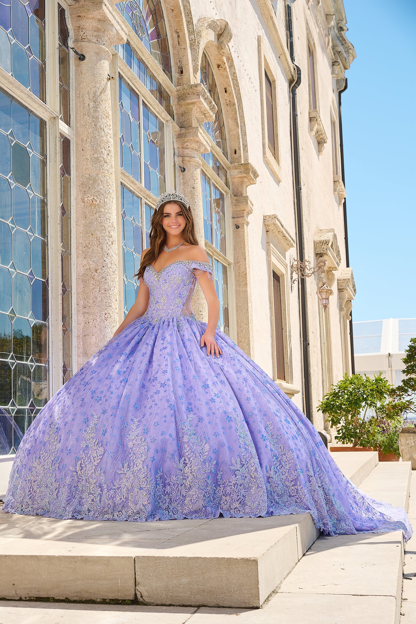 Be the belle of the ball in the Amarra 54220 Quinceanera Ball Gown. This stunning formal dress features a sheer crystal lace train and fringe, for a unique and eye-catching look. The off the shoulder design adds a touch of elegance and the perfect amount of skin. Stand out in style. Unleash your inner princess with our enchanting lace ball gown! Crafted with a dreamy lace fabric adorned with detailed floral pattern