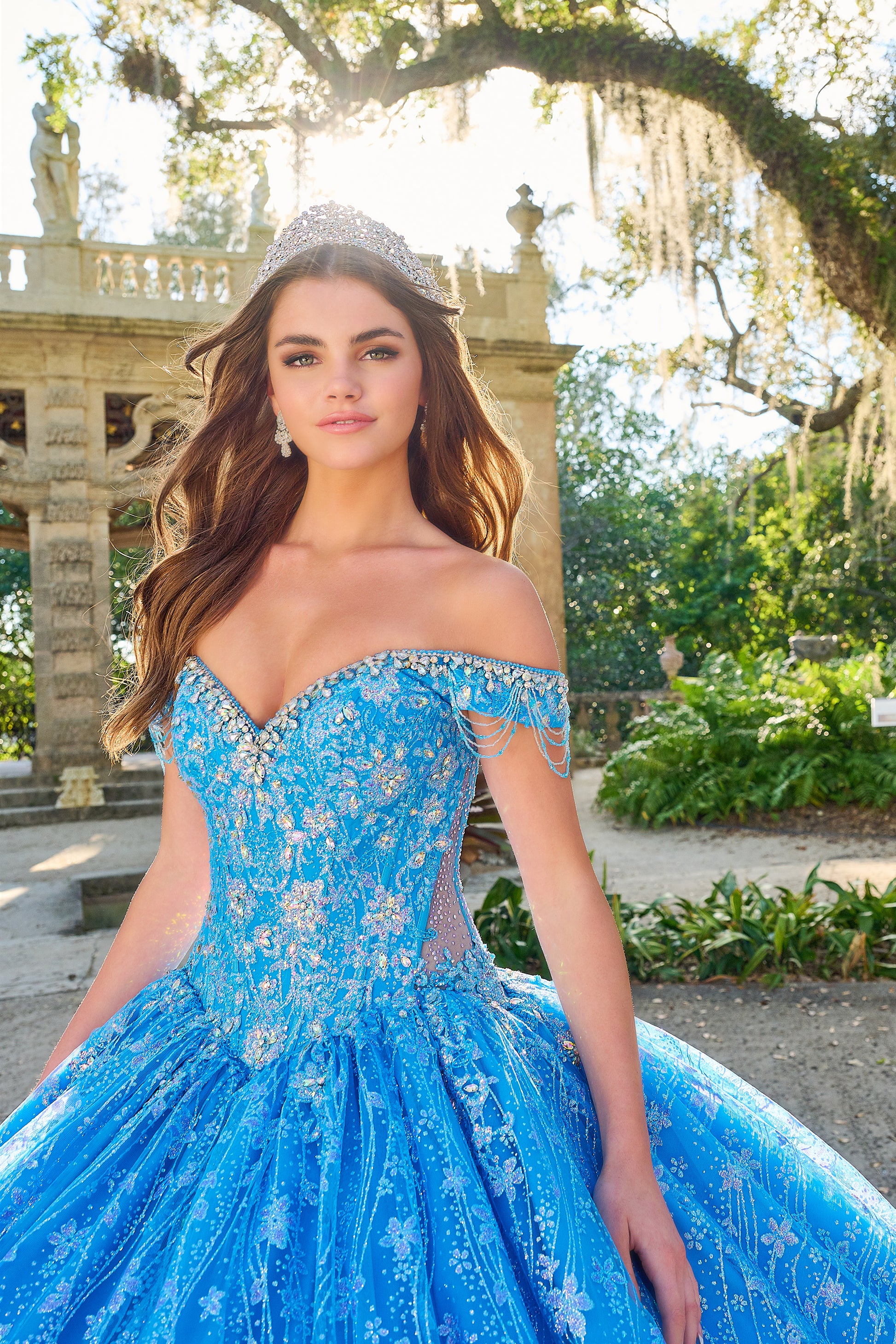 Be the belle of the ball in the Amarra 54220 Quinceanera Ball Gown. This stunning formal dress features a sheer crystal lace train and fringe, for a unique and eye-catching look. The off the shoulder design adds a touch of elegance and the perfect amount of skin. Stand out in style. Unleash your inner princess with our enchanting lace ball gown! Crafted with a dreamy lace fabric adorned with detailed floral pattern