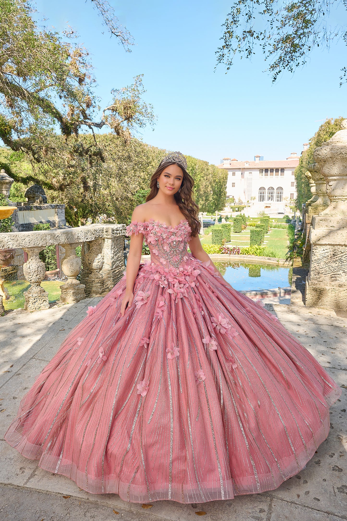 Turn heads and capture hearts in this Amarra 54226 breathtakingly whimsical ball gown! Crafted with exquisite layers of frayed tulle, this full-length dress boasts a feathery, dimensional look that's sure to enchant. The semi-sweetheart neckline paired with charming off-the-shoulder sleeves creates a delicate, feminine frame, accentuated by a fitted waistline that beautifully defines your silhouette. 