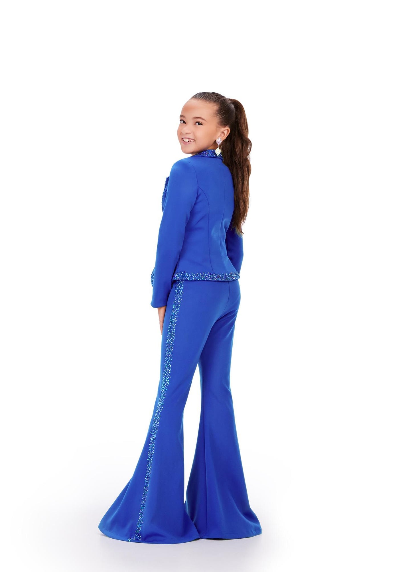 The Ashley Lauren Kids 8209 Two Piece Jumpsuit Suit features bell-bottom trousers and a crystal-studded jacket for a fashionable pageant look. High-quality materials ensure long-lasting comfort and style. Strike a pose in this fun and fabulous two piece set! Made from scuba, this suit has press on stones that trim the jacket and pant legs.  Two Piece Press On Stone Trim Flare Pant Legs Jumpsuit Sizes: 2-16 Colors: Black, Fuchsia, Royal Blue