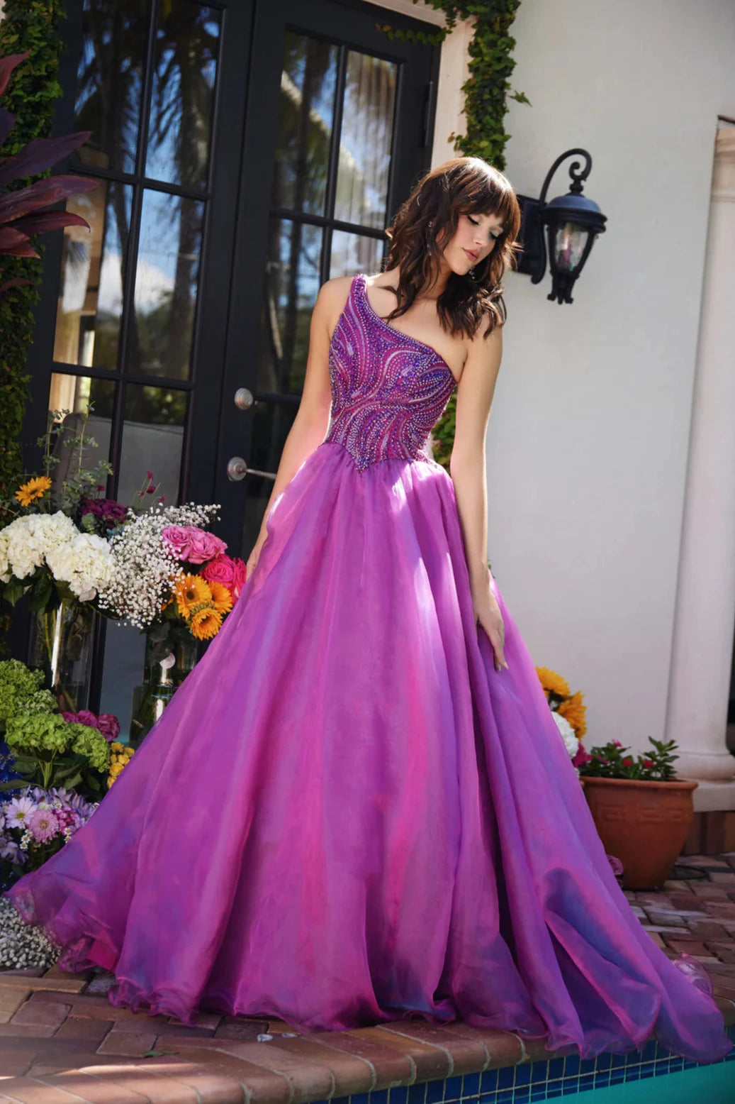 This Ava Presley gown, style 29258, exudes a captivating elegance with its magenta hue and one-shoulder design. The asymmetrical neckline adds a modern touch, while the fitted bodice features intricate beadwork in swirling patterns that accentuate the curves and create a sparkling effect.&nbsp;The full skirt is crafted from layers of lightweight fabric that flow gracefully, adding movement and volume to the gown. This design is perfect for formal events like proms, pageants, or gala evenings, offering a ble