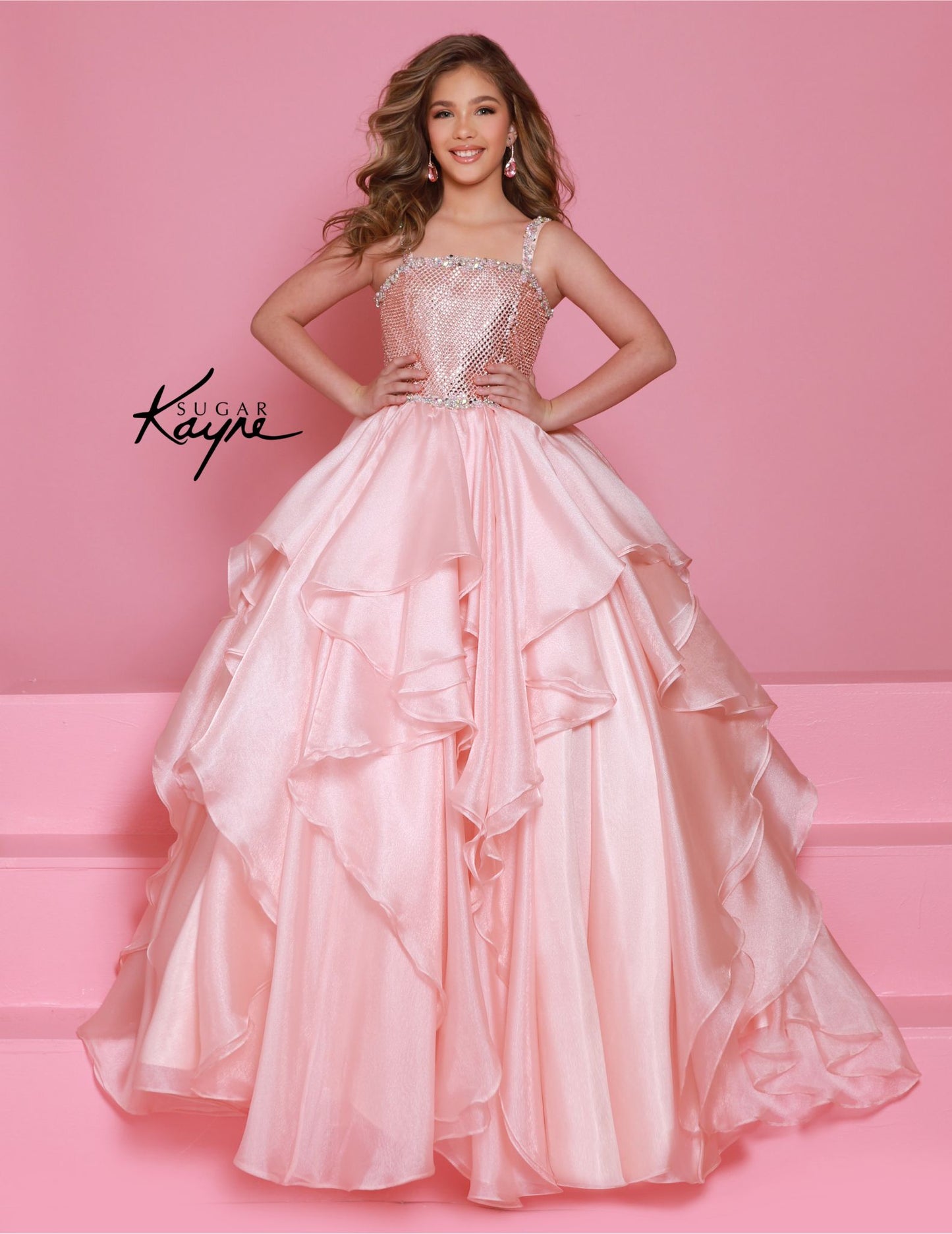 Step onto the pageant stage with confidence in the Sugar Kayne C383 Girls Pageant Dress. This stunning ballgown features a crystal bodice that will shimmer and shine under the lights, while the ruffle detail adds a touch of playful elegance. The layered skirt adds volume and movement, making you the star of the show. Make a dramatic statement at your next pageant with this stunning diamond mesh dress. The ruffled shimmer organza skirt completes the look, offering a perfect blend of elegance and flair.

Size