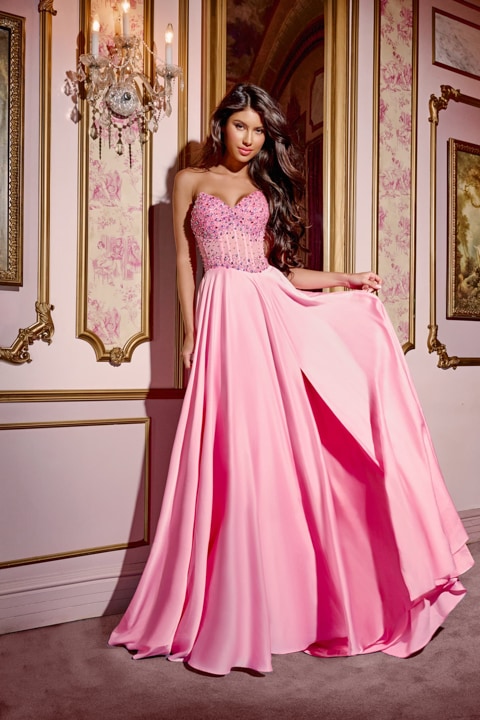 This Jovani D6021 floor-length gown features a structured sweetheart neckline, offering a flattering silhouette with its sleeveless design. The bodice is intricately embellished with scattered rhinestone accents that provide a delicate yet detailed appearance. The back of the dress is fitted and closed. The A-line skirt flows seamlessly from the fitted bodice into a voluminous chiffon train, creating graceful movement. The full-length chiffon skirt has a soft, flowing drape that enhances the dress’s airy ae