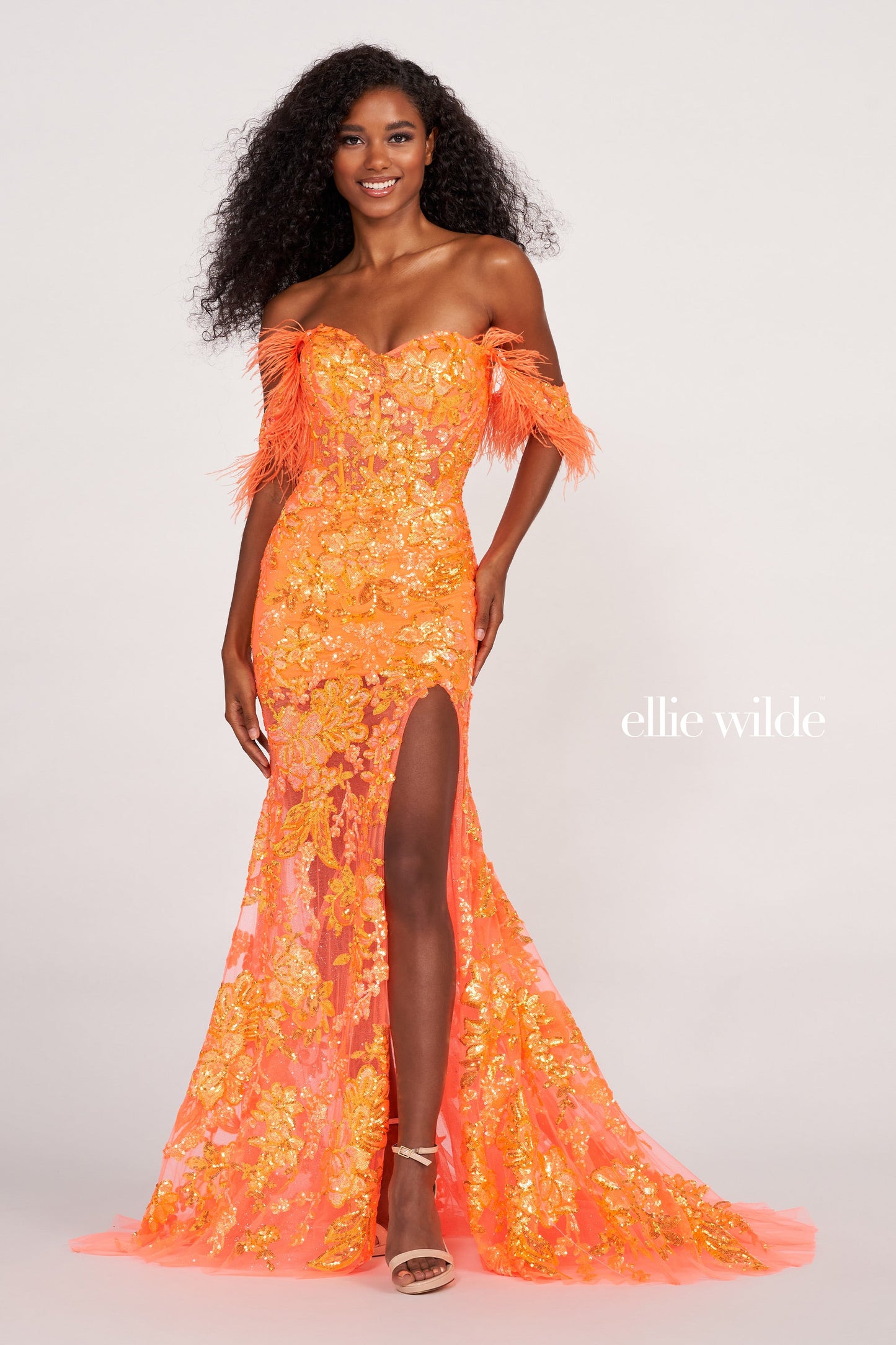 The Ellie Wilde EW34034 is a glamorous formal gown featuring an off-the-shoulder neckline, corset bodice, and a full-length sheer sequin skirt with a side slit. Festooned with a beautiful feather trim, this dress is sure to make a statement.  Sizes: 00-16  Colors: ORANGE, ROYAL BLUE, LILAC, HOT PINK, SAPPHIRE, SKY BLUE, EMERALD, PURPLE RAIN