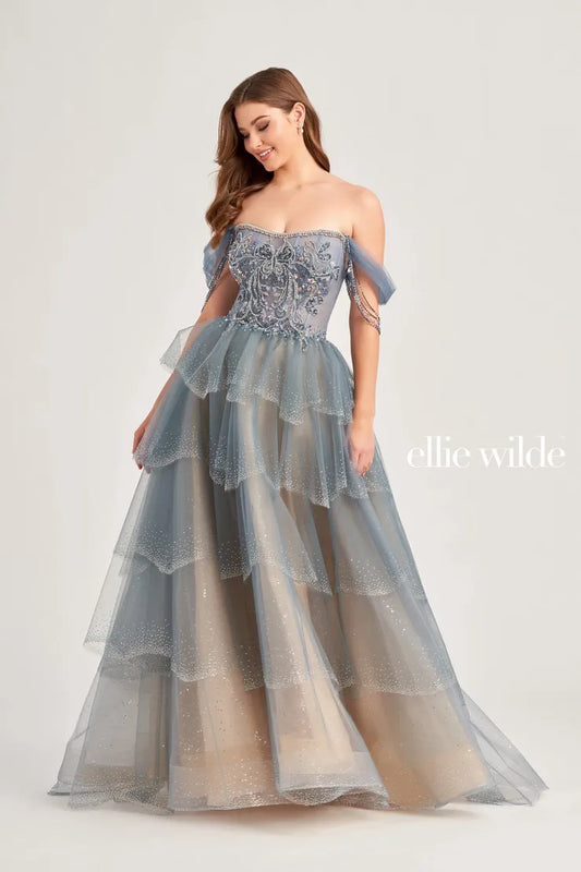 The Ellie Wilde EW35040 prom dress boasts a stunning A-line silhouette adorned with sparkling crystals and sequins. The sheer corset bodice adds a touch of allure, while the off-the-shoulder neckline and beaded fringe details add a trendy touch. Elevate your prom look with this enchanting and figure-flattering dress.  Sizes: 00-16  Colors: Slate, Black/Champagne