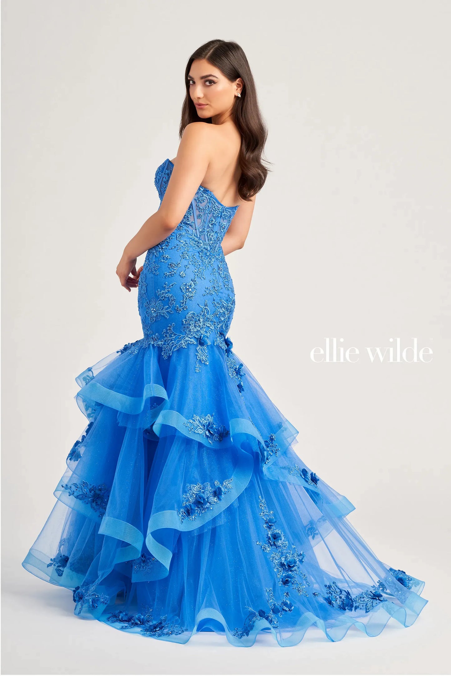 Get ready to make a statement in this Ellie Wilde EW35239 mermaid prom dress. The sheer corset lace bodice is adorned with embroidered and glitter tulle, while the ruffle layer skirt shimmers with stone accents and 3D flowers. You'll be the belle of the ball in this stunning dress.  Sizes: 00-16  Colors: Ocean Blue, Lilac, Red