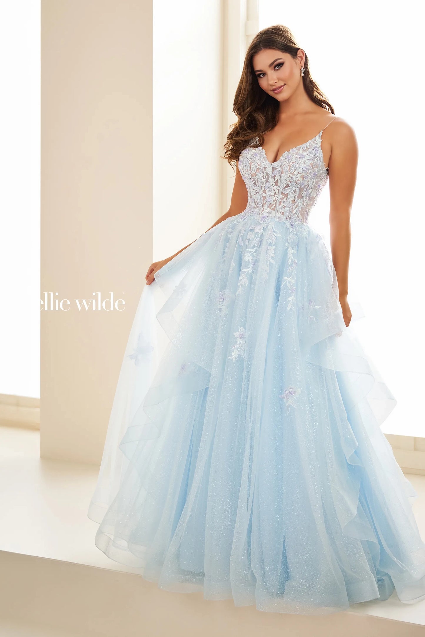 This Ellie Wilde EW3685 dress features sheer lace and a shimmering design for a glamorous look. The A-line silhouette flatters all body types, while the ruffle detailing adds a touch of elegance. Perfect for prom, formal events, and pageants.