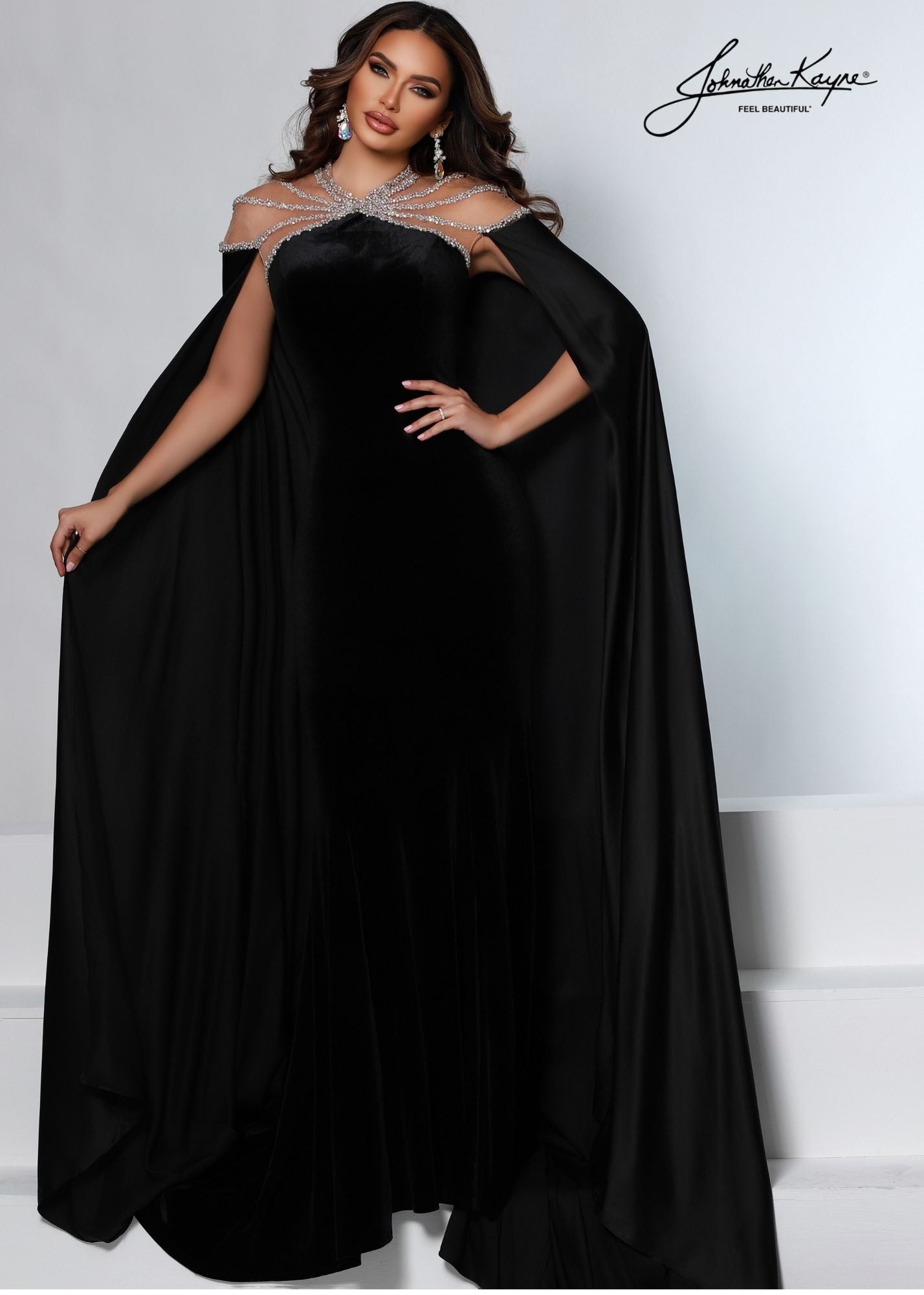 Johnathan Kayne 2535 Long Fitted Velvet Pageant Dress Cape Sheer Crystal Prom Gown A true showstopper! This velvet gown with high neck mesh bodice and sewn in charmeuse skirt will flow across your next pageant stage.  Colors: Emerald, Royal, Black  Sizes: 00, 0, 2, 4, 6, 8, 10, 12, 14, 16, 18  Fabric Stretch Velvet, Stretch Lining