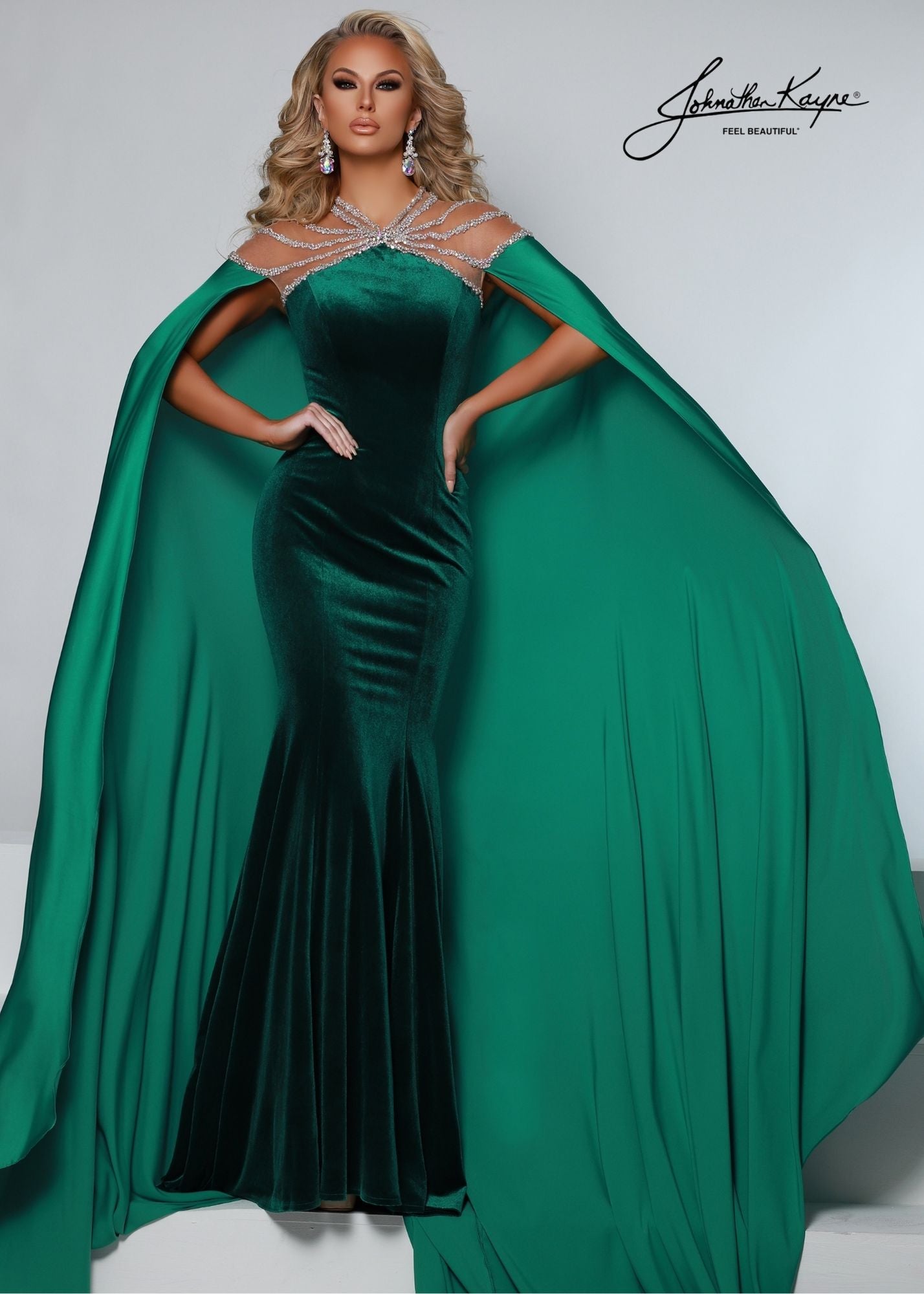 Johnathan Kayne 2535 Long Fitted Velvet Pageant Dress Cape Sheer Crystal Prom Gown A true showstopper! This velvet gown with high neck mesh bodice and sewn in charmeuse skirt will flow across your next pageant stage.  Colors: Emerald, Royal, Black  Sizes: 00, 0, 2, 4, 6, 8, 10, 12, 14, 16, 18  Fabric Stretch Velvet, Stretch Lining