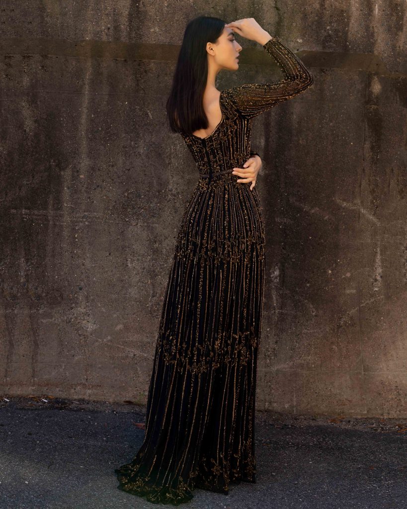 Primavera Couture 3685 This long beaded evening gown has a bateau neckline and long embellished sleeves.  The A line design is beaded to the floor and has a boho tone. Available colors:  Champagne, Black Multi  Available sizes:  0-24