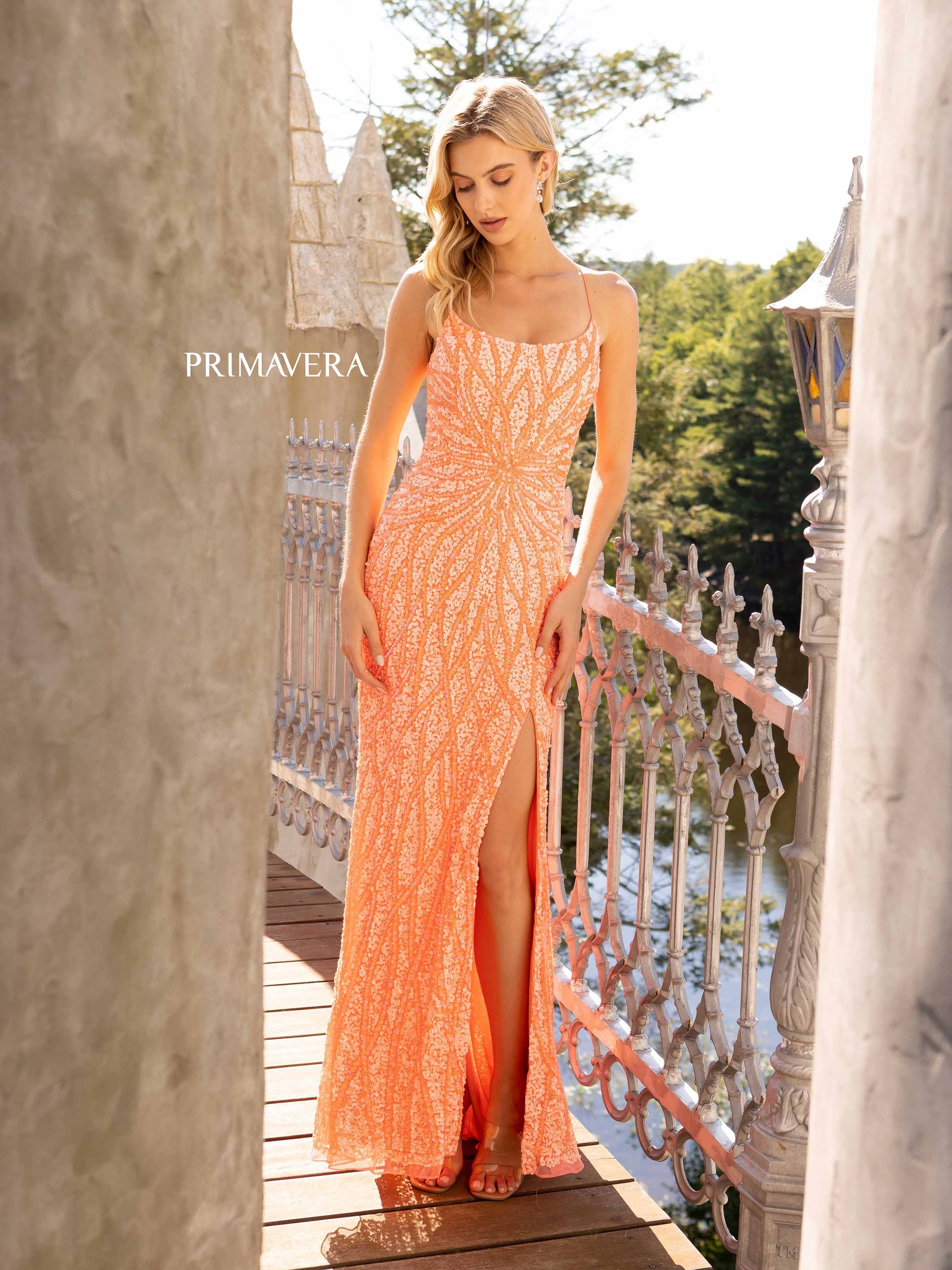 Primavera Couture 3959 This is a coral fully sequined prom dress.  It features a starburst in the front of the dress with waterfall streaming sequins up and down the long length of the dress.  It has a corset open back and a side slit,  Available Size: 2, 10   Available Colors: Coral