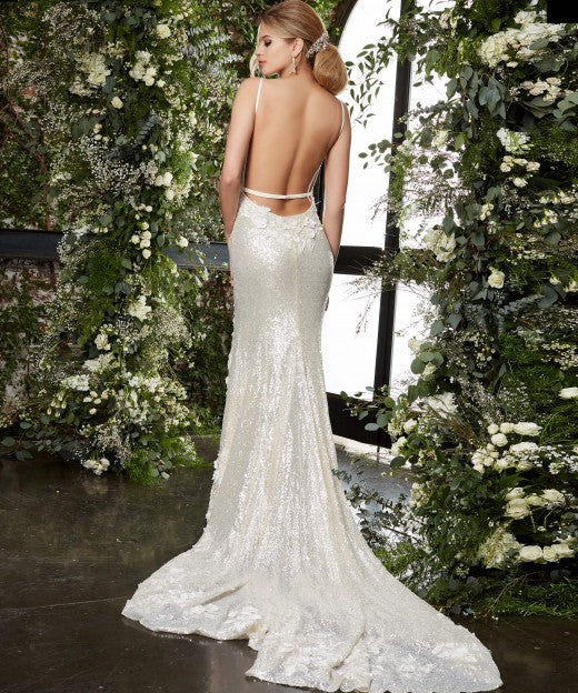 Jovani Bridal JB03592 cream bridal gown features a slim silhouette with a deep plunging neckline, spaghetti straps and a single-strap open back. Three-dimensional floral appliques embellish this sequin wedding dress, finished with a thigh-high slit and a chapel train. Sequin Floral Lace Backless Wedding Dress Slit Train Fitted  Available Sizes: 00-24  Available Colors: Cream